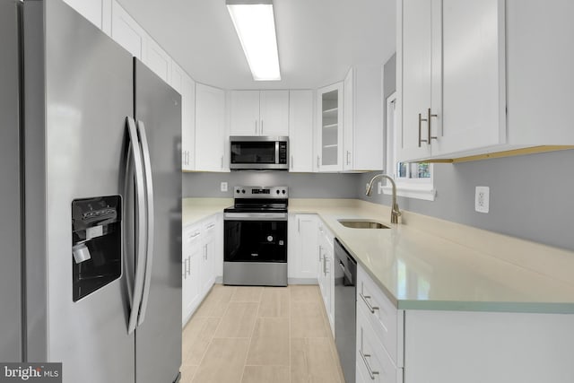 kitchen featuring a sink, light countertops, glass insert cabinets, stainless steel appliances, and white cabinetry