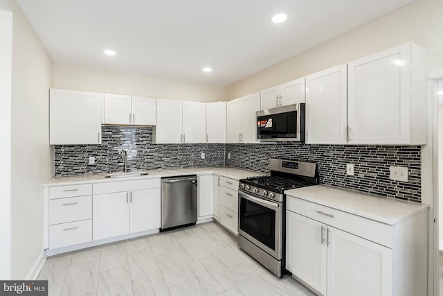 kitchen featuring tasteful backsplash, white cabinets, appliances with stainless steel finishes, light countertops, and a sink