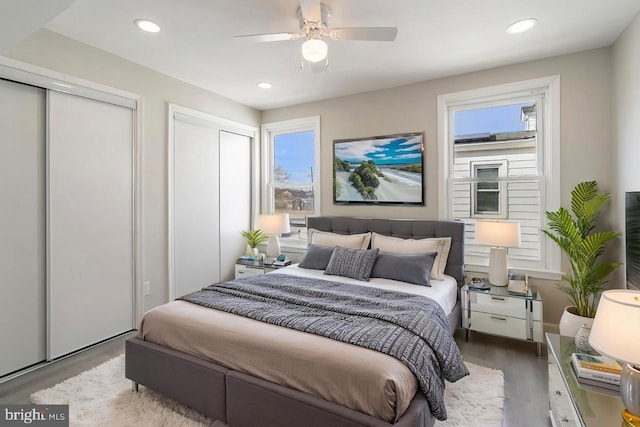bedroom featuring two closets, wood finished floors, ceiling fan, and recessed lighting