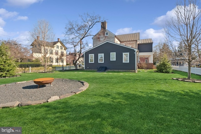 rear view of property with a standing seam roof, a chimney, metal roof, fence, and a yard