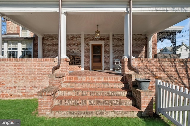 view of exterior entry featuring a porch and brick siding