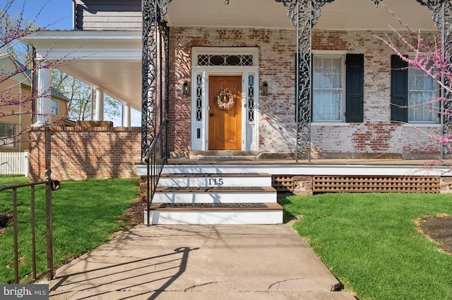 property entrance featuring a porch, brick siding, and a yard