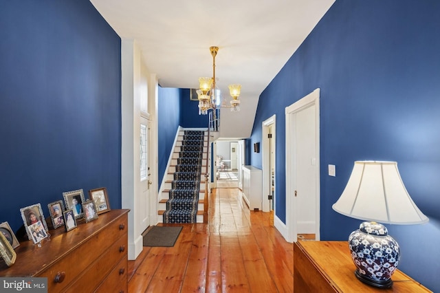 hallway with an inviting chandelier, baseboards, stairway, and hardwood / wood-style flooring