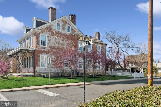view of side of home featuring fence, a chimney, a yard, and brick siding