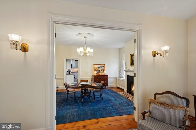 dining space with a fireplace with flush hearth, baseboards, wood finished floors, and a chandelier