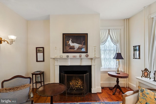 sitting room with a healthy amount of sunlight, a fireplace with flush hearth, baseboards, and wood finished floors