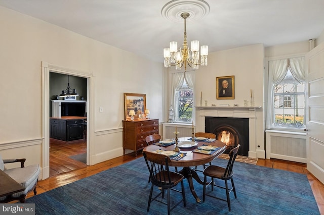 dining space with an inviting chandelier, a fireplace with flush hearth, wood finished floors, and radiator