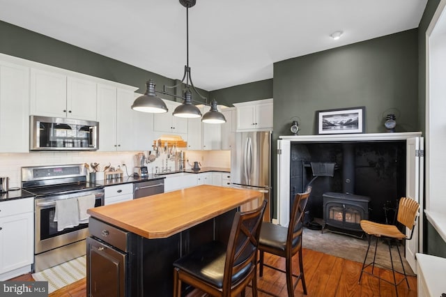 kitchen with a wood stove, a breakfast bar area, stainless steel appliances, decorative backsplash, and wood finished floors