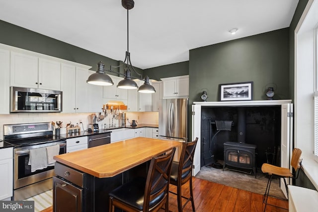 kitchen with dark wood-style flooring, appliances with stainless steel finishes, a wood stove, white cabinetry, and butcher block countertops
