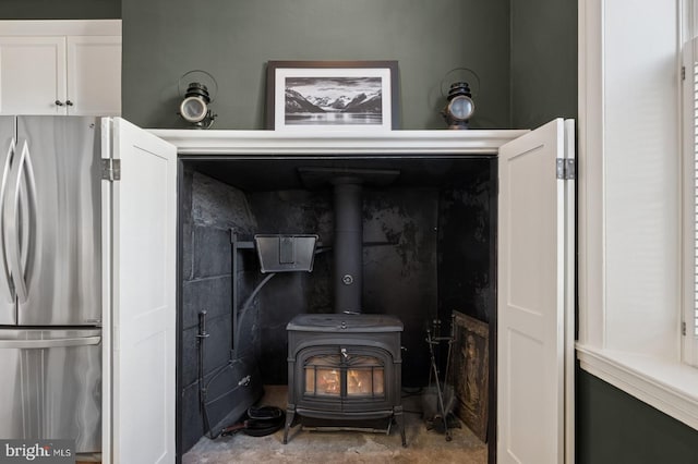 details with freestanding refrigerator, a wood stove, and concrete floors