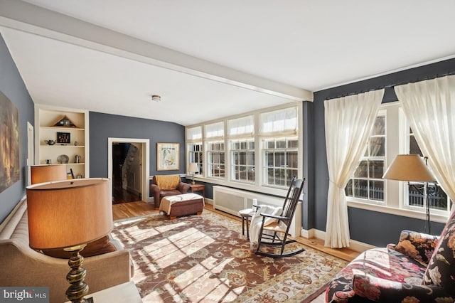 living area featuring beam ceiling, built in features, radiator heating unit, baseboards, and wood finished floors