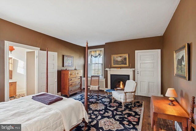 bedroom featuring a warm lit fireplace, wood finished floors, and radiator