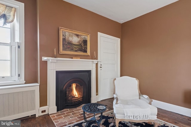 sitting room featuring baseboards, radiator heating unit, a warm lit fireplace, and wood finished floors