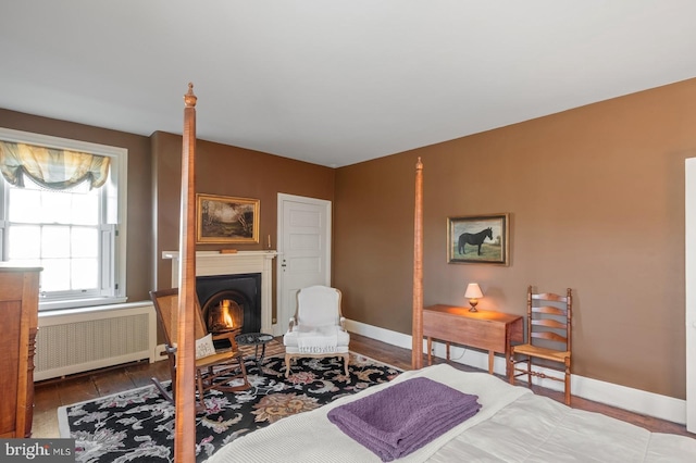 bedroom with baseboards, radiator heating unit, and a warm lit fireplace