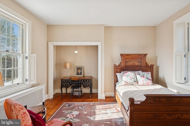 bedroom featuring radiator heating unit, baseboards, and wood finished floors
