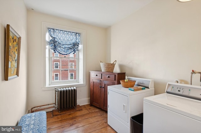 clothes washing area featuring radiator, light wood-style floors, baseboards, washer and clothes dryer, and cabinet space