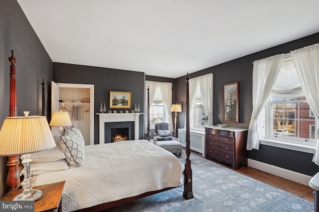 bedroom featuring radiator heating unit, baseboards, a warm lit fireplace, and wood finished floors