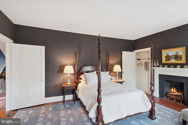 bedroom with baseboards, a closet, a warm lit fireplace, and wood finished floors