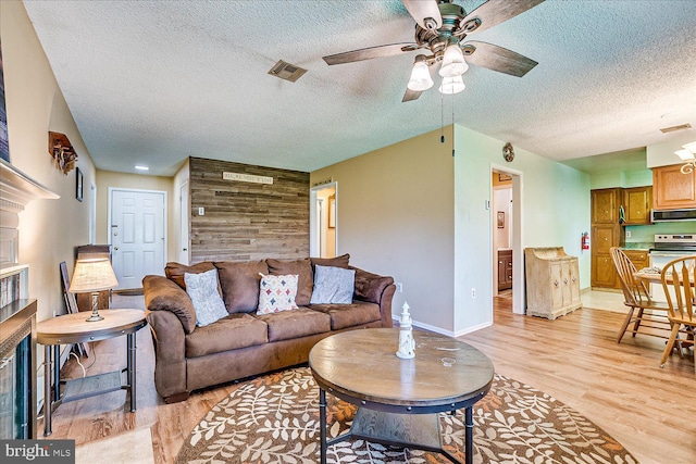 living area featuring ceiling fan, a textured ceiling, visible vents, a fireplace, and light wood finished floors