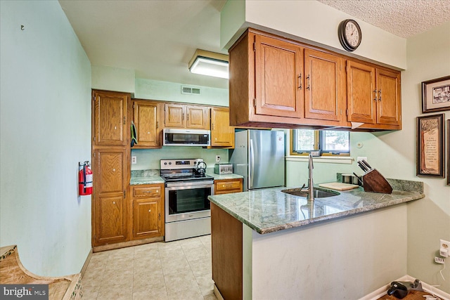 kitchen featuring visible vents, brown cabinets, a sink, a peninsula, and stainless steel appliances