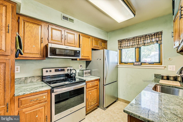 kitchen with a sink, appliances with stainless steel finishes, brown cabinets, and visible vents