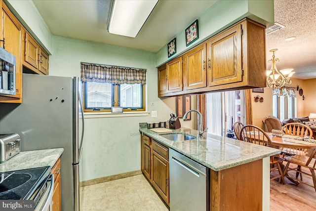 kitchen featuring brown cabinets, appliances with stainless steel finishes, a sink, and an inviting chandelier