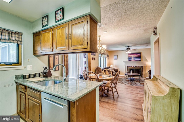 kitchen with brown cabinetry, a glass covered fireplace, a sink, light wood finished floors, and dishwasher