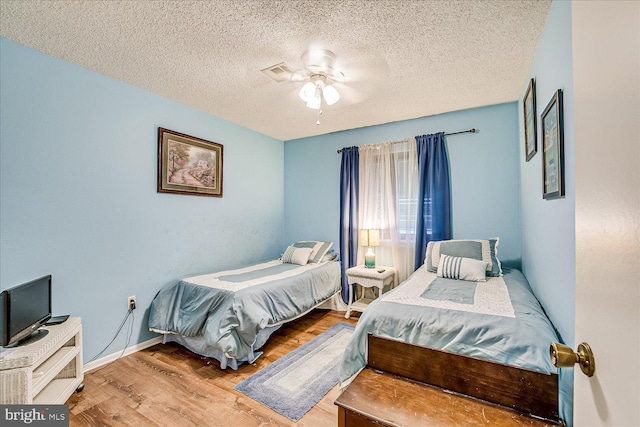 bedroom featuring ceiling fan, a textured ceiling, baseboards, wood finished floors, and visible vents