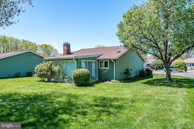 rear view of property featuring roof with shingles, a yard, and a chimney