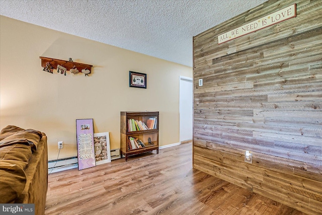 interior space with wooden walls, baseboard heating, a textured ceiling, and wood finished floors