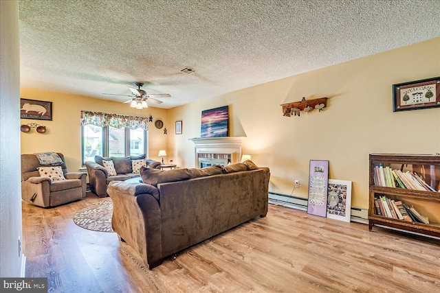 living area with visible vents, wood finished floors, a textured ceiling, a baseboard heating unit, and a ceiling fan