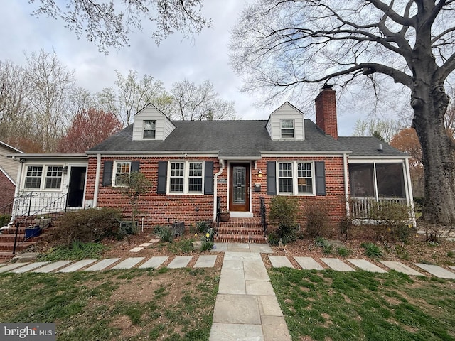 new england style home with a sunroom, a shingled roof, a chimney, and brick siding