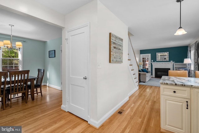 interior space with baseboards, a chandelier, light wood-style floors, stairs, and a fireplace