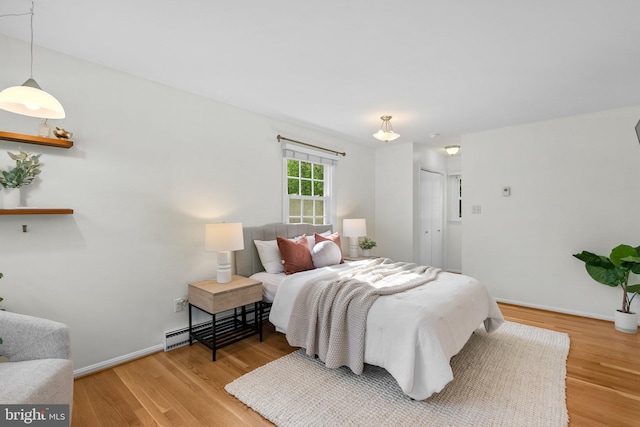 bedroom featuring a baseboard heating unit, wood finished floors, a closet, and baseboards