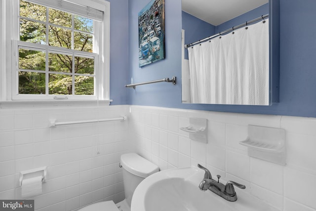 full bathroom with toilet, a sink, tile walls, wainscoting, and a shower with shower curtain