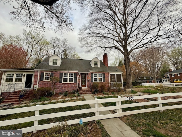 new england style home featuring a chimney, brick siding, and a fenced front yard