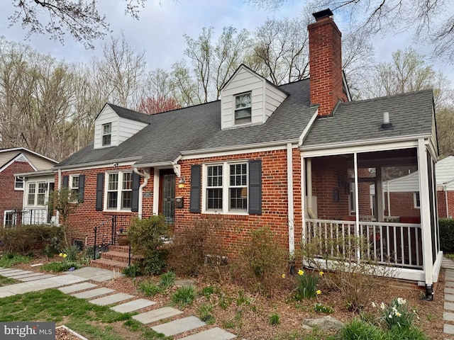 cape cod home with brick siding, a sunroom, a shingled roof, and a chimney