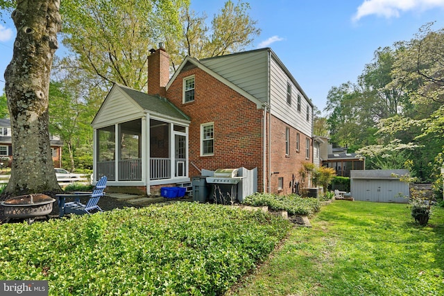 rear view of house featuring a fire pit, a chimney, brick siding, a yard, and a sunroom