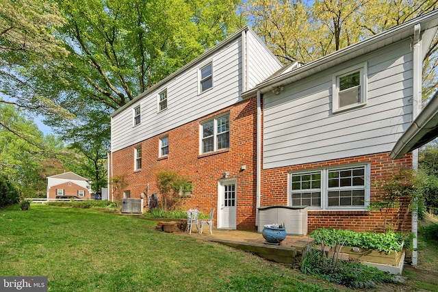 back of house featuring brick siding, a lawn, and central AC unit