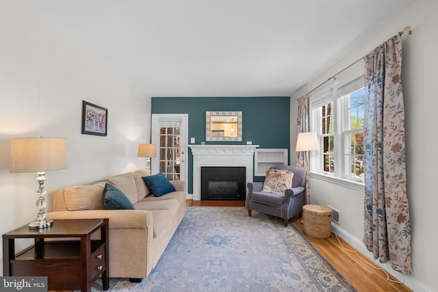 living area featuring baseboards, a brick fireplace, and wood finished floors