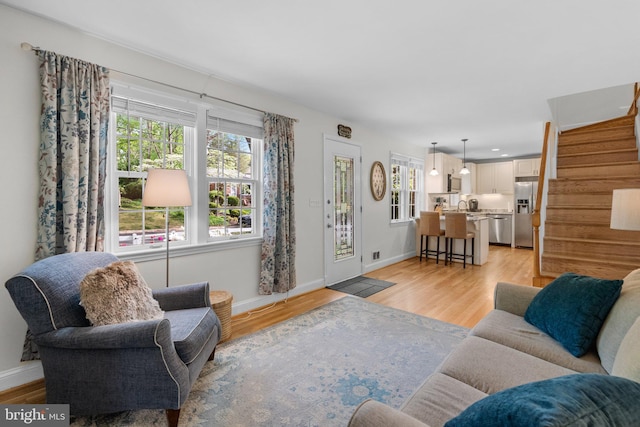 living room featuring plenty of natural light, baseboards, light wood-style floors, and stairway