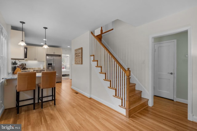 kitchen featuring a peninsula, baseboards, light wood-style floors, pendant lighting, and stainless steel fridge with ice dispenser