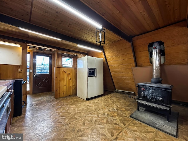 kitchen featuring white fridge with ice dispenser, a wood stove, wood ceiling, stove, and wood walls