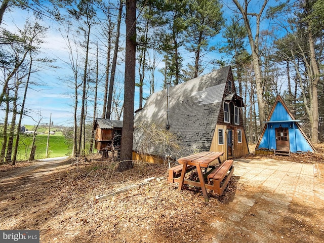 view of home's exterior with a gambrel roof, roof with shingles, and an outbuilding