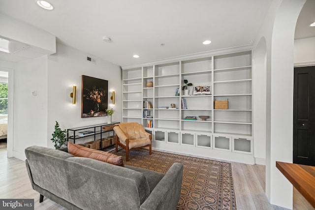 living area with recessed lighting, arched walkways, built in features, and wood finished floors