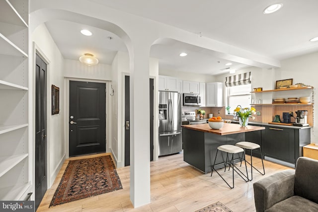 kitchen with open shelves, appliances with stainless steel finishes, a breakfast bar, light wood-style floors, and butcher block counters