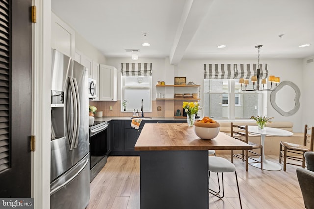 kitchen with appliances with stainless steel finishes, plenty of natural light, butcher block counters, and a notable chandelier