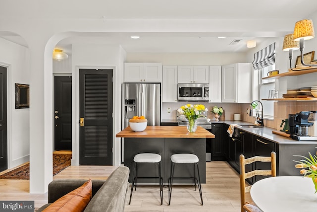 kitchen featuring white cabinets, open shelves, appliances with stainless steel finishes, a sink, and wooden counters