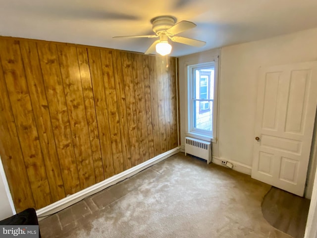 spare room with radiator, baseboards, ceiling fan, wooden walls, and carpet