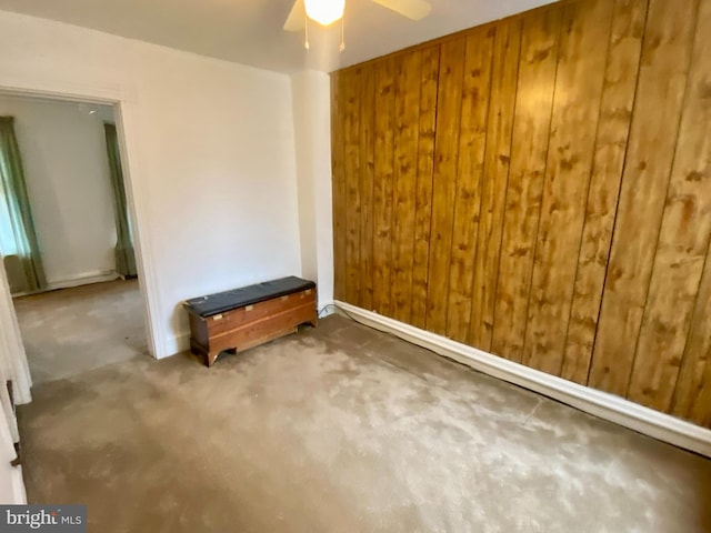 carpeted empty room with wooden walls and a ceiling fan